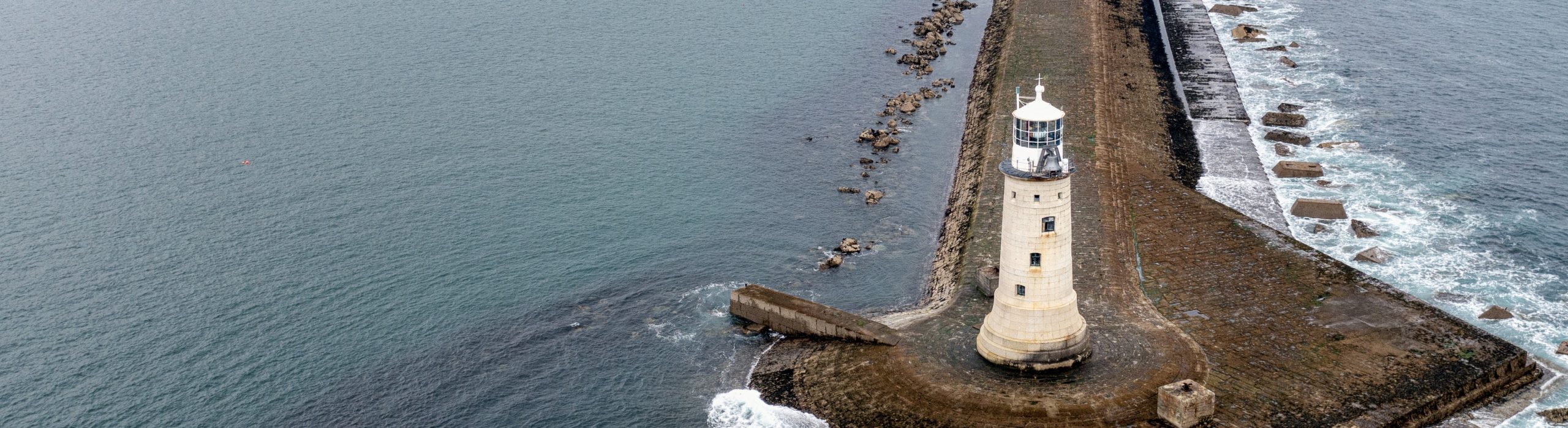 Aerial view of a lighthouse on a breakwater, surrounded by the sea.